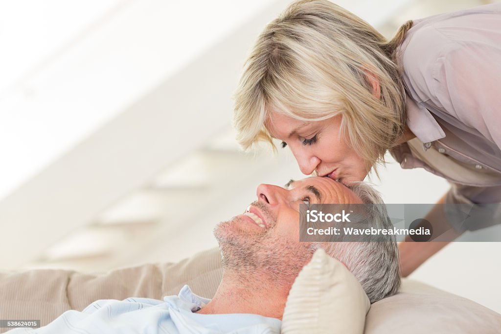 Side view of a woman kissing relaxed mature man Side view of a woman kissing a relaxed mature mans forehead in the living room at home 2015 Stock Photo