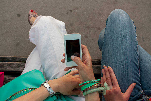 istock two women sitting on the bench and using smartphone 538641552