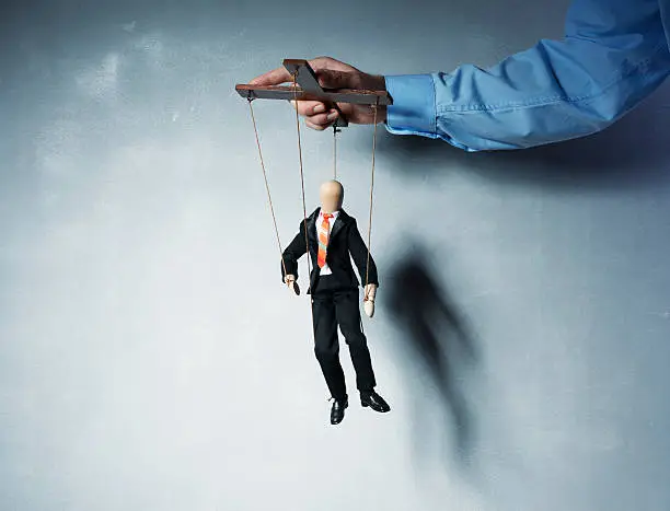 Businessman's hand controlling a worker marionette.