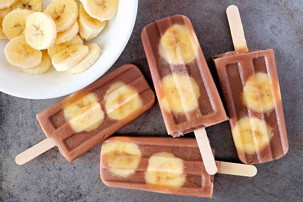 Chocolate banana popsicles on rustic grey background Chocolate banana popsicles in a cluster with sliced bananas on rustic grey background homemade icecream stock pictures, royalty-free photos & images