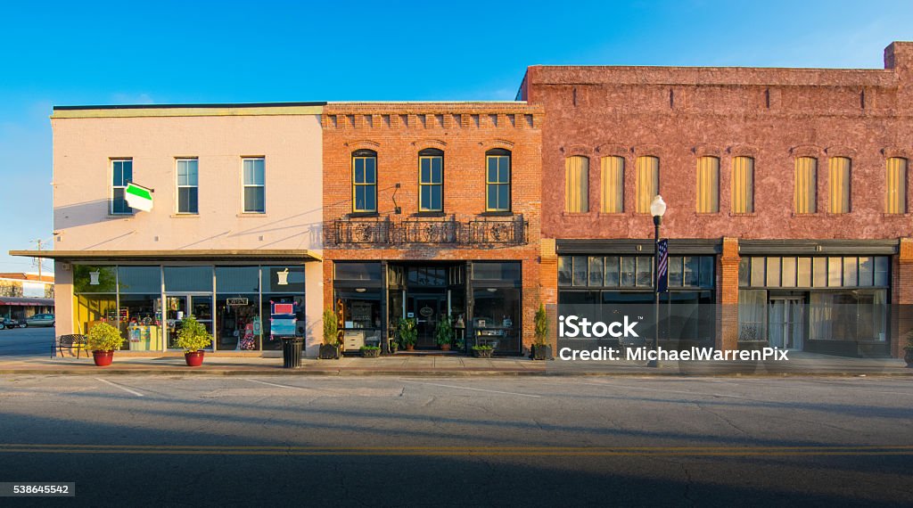 Row of Old Shops in Small Town Storefront facades at dusk on a quiet street in a small Georgia town. The scene includes small retail shops in the evening light against a deep blue sky. The street and parking spaces are empty. Store Stock Photo