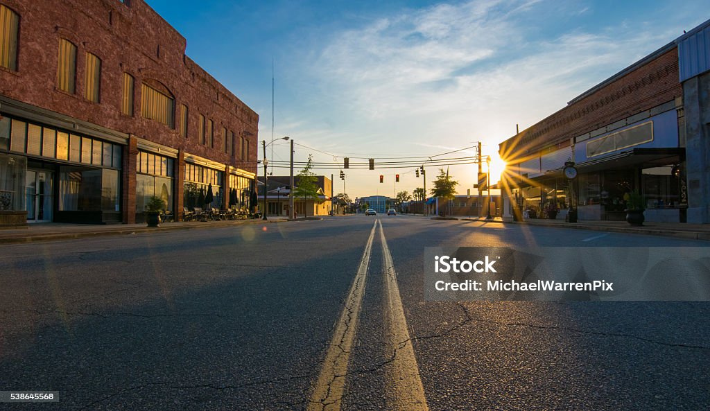 Sunset in Small Town Storefronts at sunset in the middle of the road in downtown in a small Georgia town. The scene includes a low-angle view of the middle divider, sunburst at sunset, deep shadows and saturated colors.  The street and parking spaces are empty. Small Town America Stock Photo