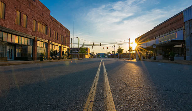 Sunset in Small Town Storefronts at sunset in the middle of the road in downtown in a small Georgia town. The scene includes a low-angle view of the middle divider, sunburst at sunset, deep shadows and saturated colors. The street and parking spaces are empty. small town america stock pictures, royalty-free photos & images