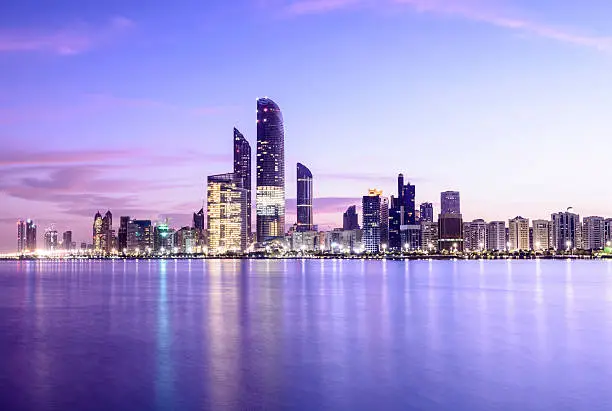 Abu Dhabi city skyline at twilight with reflection in the still sea, United Arab Emirates.