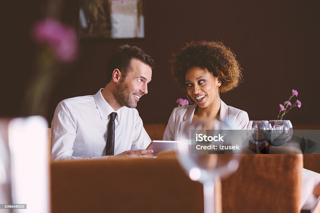 Businesswoman and businessman on lunch Businesswoman and businessman talking during lunch in restaurant, man holding digital tablet. Women Stock Photo
