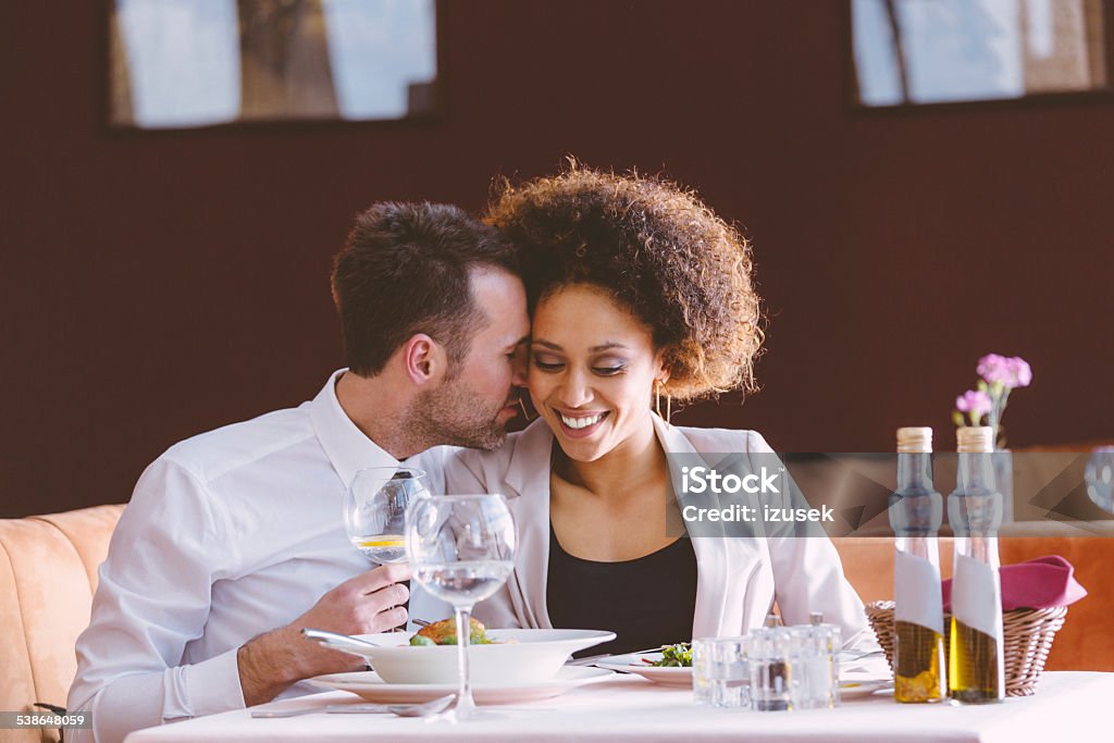 Flirting couple on lunch Cheerful businesswoman and businessman flirting during lunch in the restaurant, sitting at the table, man whispering into woman's ear. 2015 Stock Photo