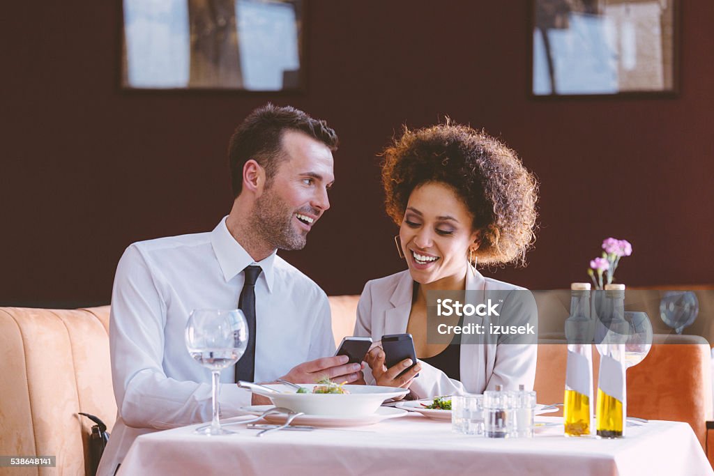 Businessman and businesswoman on lunch Cheerful businesswoman and businessman having lunch in the restaurant, using smart phones together. Couple - Relationship Stock Photo