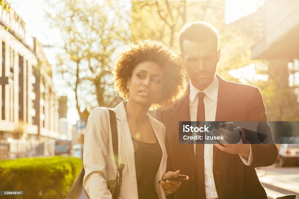 Outdoor portrait of two business people with smart phones Outdoor portrait of businessman and businesswoman using a smart phones at sunset. Suit Stock Photo
