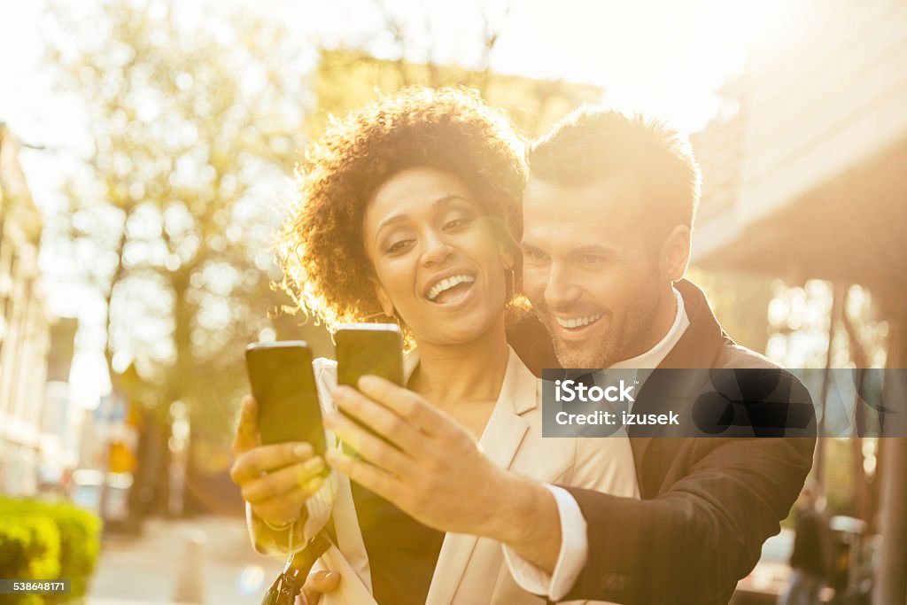 Two business people taking selfie Outdoor portrait of cheerful businessman and businesswoman taking selfie using a smart phones at sunset. 2015 Stock Photo