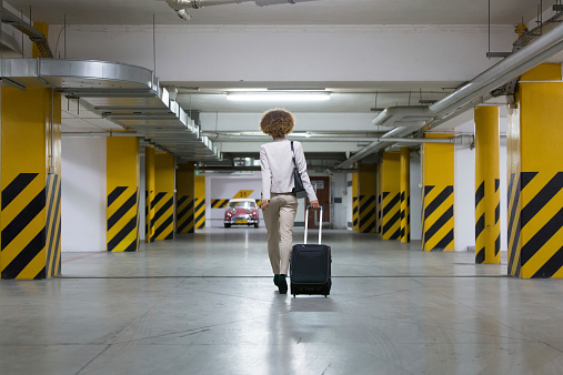 Back view of businesswoman walking on the underground parking and carrying suitcase.