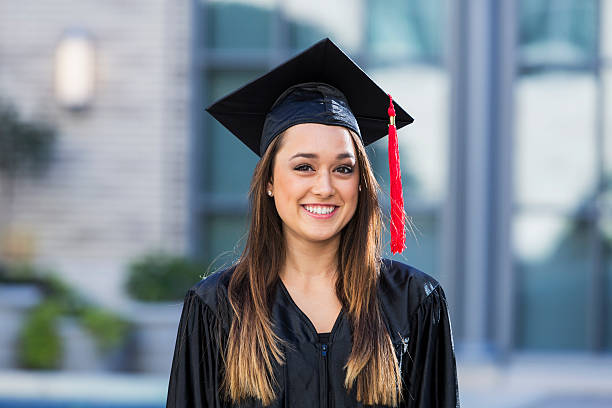 A young woman wearing a cap and gown, mixed race Hispanic and Caucasian.  She is a university or high school graduate, smiling at the camera.