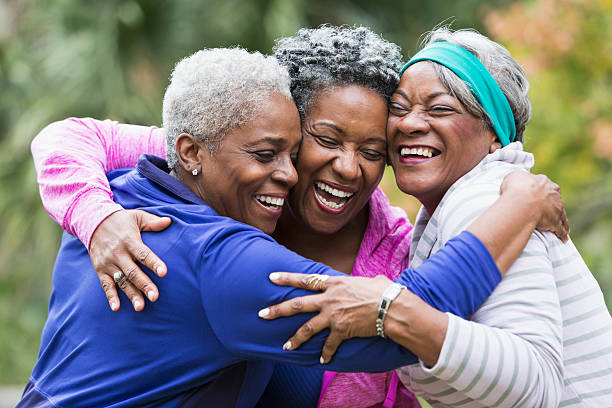 Three seniors hugging Three senior African American women at the park, hugging.  They are best friends excited to see each other. Their eyes are closed and they are smiling and laughing. cheek to cheek photos stock pictures, royalty-free photos & images