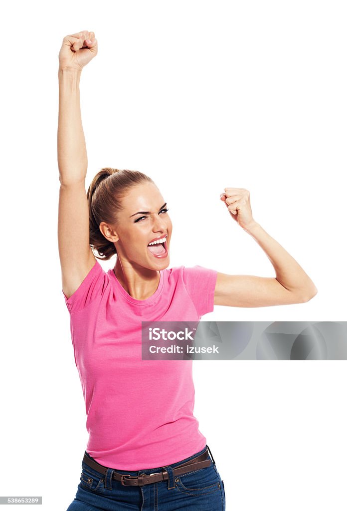 Excited young woman with raised fists, Studio Portrait Portrait of excited young woman wearing pink t-shirt, laughing at camera with raised fists. Studio shot, white background. Women Stock Photo