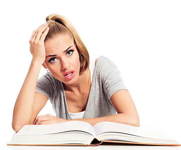 Portrait of bored young woman with book sitting at the table and looking at camera. Studio shot, isolated on white.