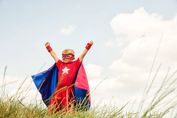 młody chłopiec przebrany za superbohatera podnosi ręce w parku - superhero child partnership teamwork zdjęcia i obrazy z banku zdjęć