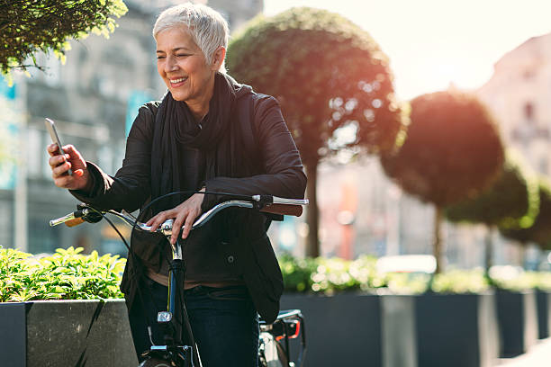 ältere frau benutzt ihr smartphone mit dem fahrrad. - short cycle stock-fotos und bilder