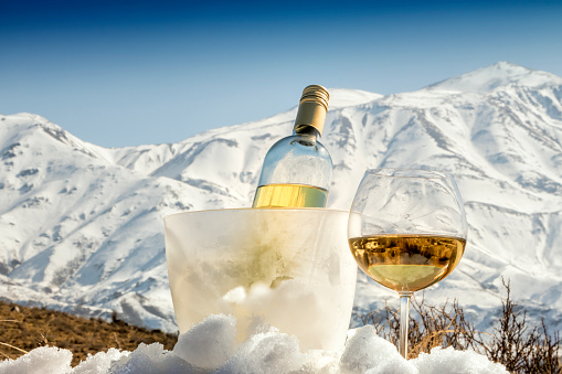 Bottle and glass of white wine, at foot of the snowy Alps. Italy.