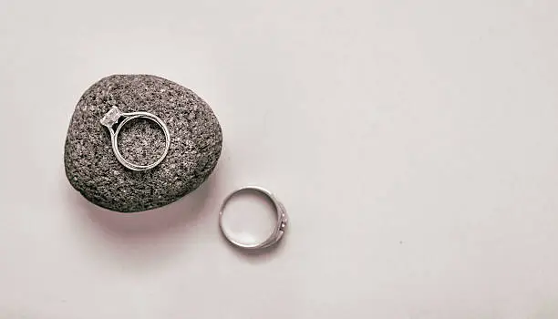His & hers wedding rings on a white background with her ring in sharp focus and sitting on a textured stone.