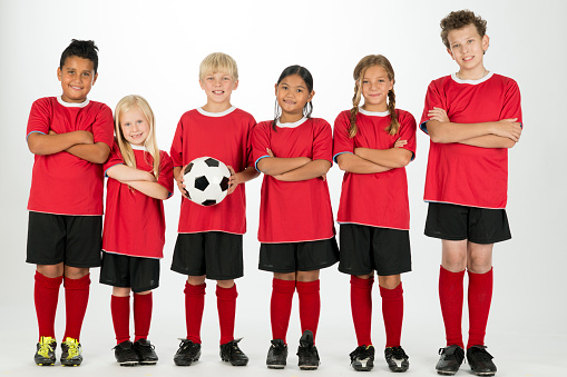 A multi-ethnic group of elementary age children are wearing their soccer uniforms and are standing in a row while smiling and looking at the camera. The picture is isolated on white.