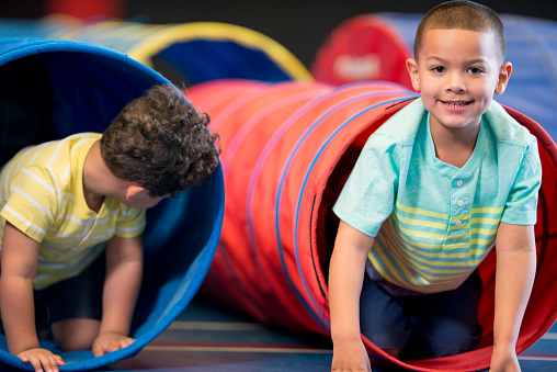 A multi-ethnic group of elementary age children are playing at recess on gym mats and tunnels.