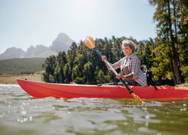 reife frau paddeln ein kajak in see - kayak canoeing canoe lake stock-fotos und bilder