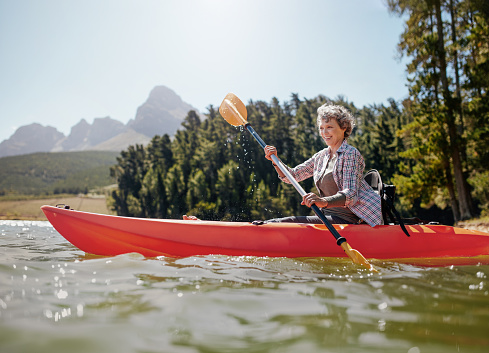 Shot of senior woman kayaking on lake on a summer day. Mature woman paddling a kayak in lake.