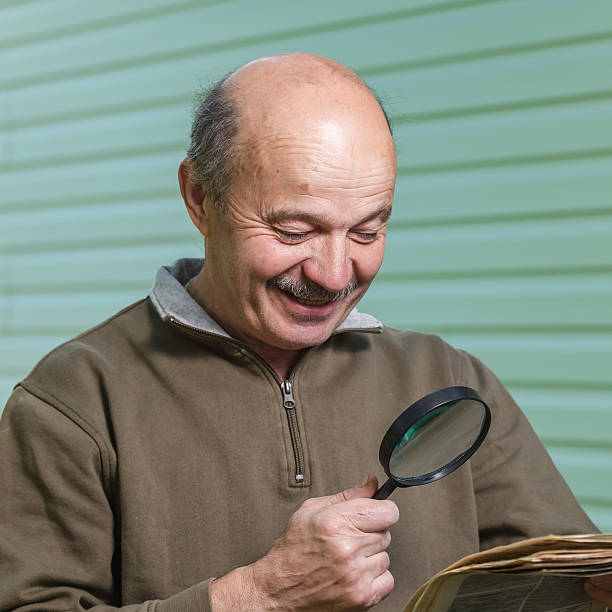 istock Pensioner reads ad in newspaper, looking through magnifying glass. 538682516