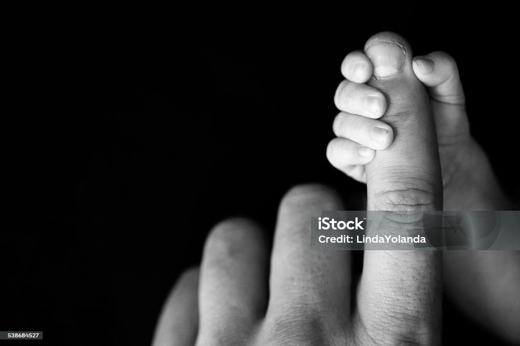 Newborn Baby's Hand Gripping Dad's Finger A close up image of a newborn baby's tiny fingers wrapped around dad's finger. Copy space in black background. Father Stock Photo