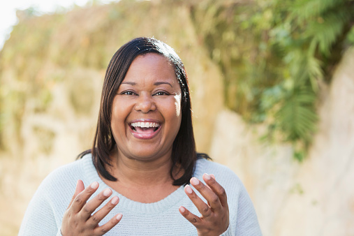 Face of a happy, mature, African American woman with a big smile, looking at the camera and gesturing with her hands.