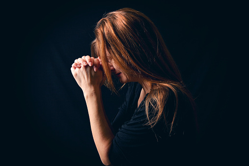 A crying woman with long red hair saying a prayer in the dark.