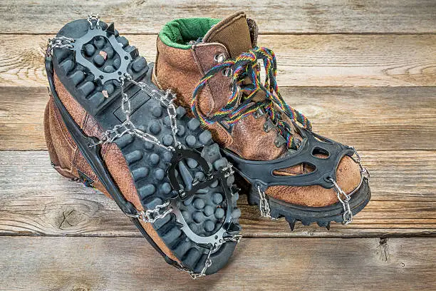 old hiking boots with trail crampons on wood background
