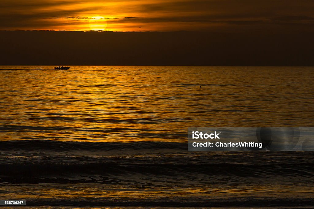 Sunset Silhouette with Sun, Clouds, Boat and Ocean A fast boat is cast in silhouette by the setting sun. The image includes the sun, a boat, and red and gold colors reflected off the clouds and the ocean's surface. Siesta Key Beach, Sarasota, Florida. 2015 Stock Photo