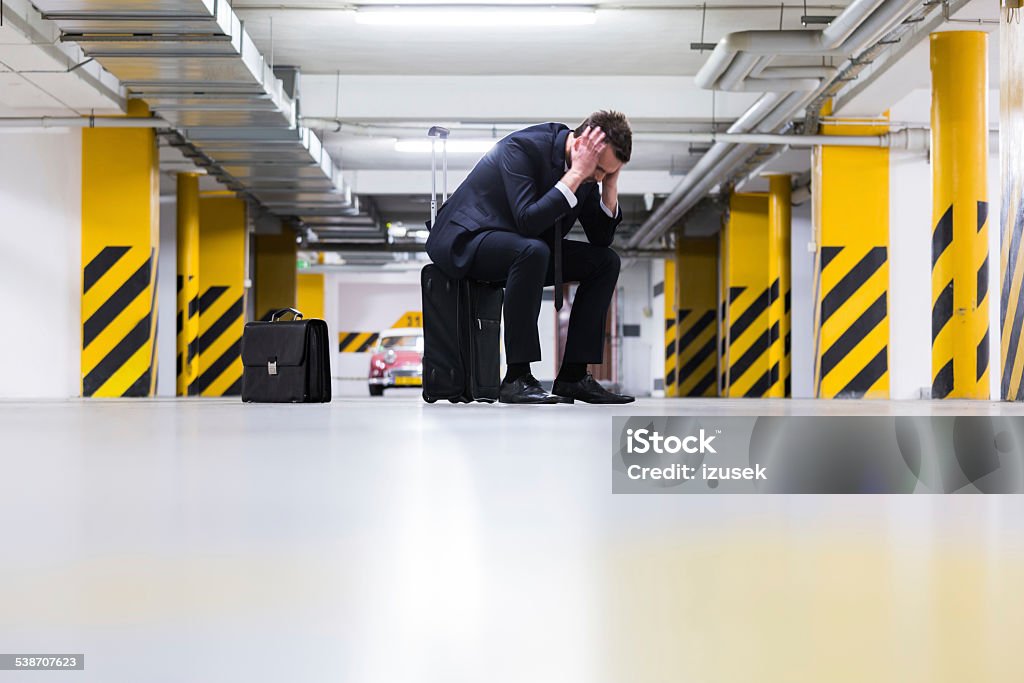 Businessman in underground garage Full lenght portrait of disappointed businesswoman sitting on the suitcase in the underground parking. Business Person Stock Photo