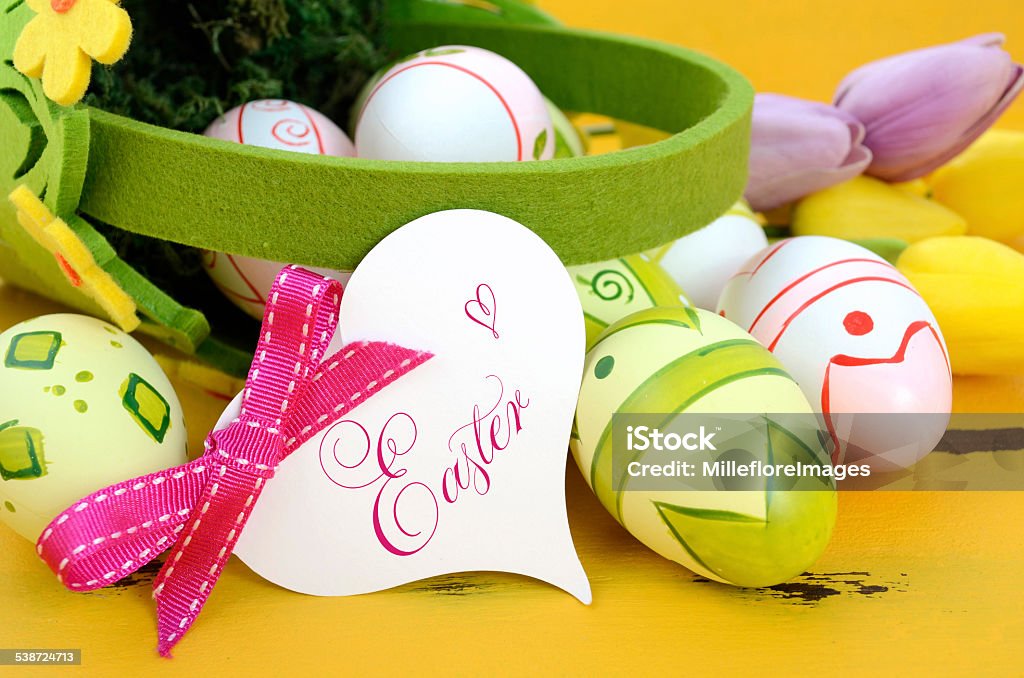 Happy Easter eggs in basket on yellow wood Happy Easter green and yellow felt basket of of pink, white and green easter eggs on rustic vintage yellow wood table, with heart shape greeting card, closeup. 2015 Stock Photo