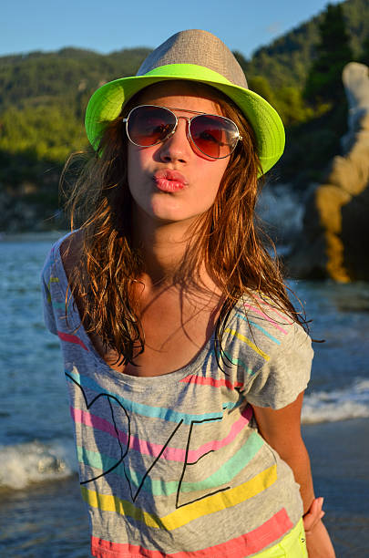 Preteen girl with hat and sunglasses in sunset light on a beach