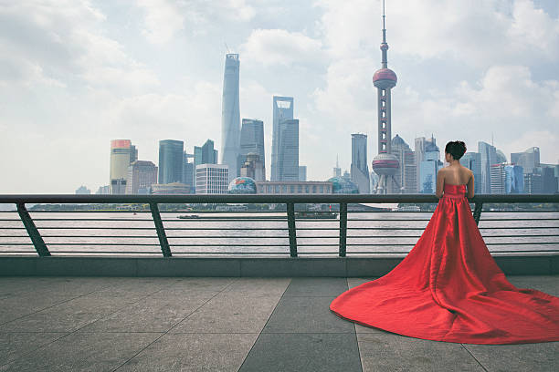 Shanghai Bride A Shagaise girl in a bridal (yes the brides traditionally wear red in China) dress looking at modern Pudong area of Shanghai from The Bund. There is only one person in this photograph and dramatic lighting. chinese wedding dress stock pictures, royalty-free photos & images