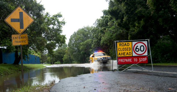 Queensland Flooded Road Cyclone Marcia Palmwoods, Australia - February 21, 2015: Image shows a flooded road with road closed ahead roadsign. Yellow rural firebrigade four wheel drive vehicle crossing the floodwater. Palmwoods, Sunshine Coast, Queensland, Australia road closed sign horizontal road nobody stock pictures, royalty-free photos & images