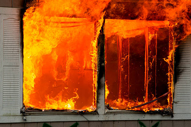 Flames erupting from window in burning home stock photo