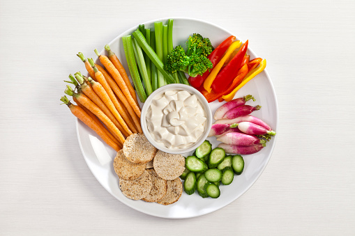 Vegetables and dip plate on white table shot from above