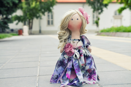 Handmade doll with natural hair in a long patchwork dress, strolling through the historic main square