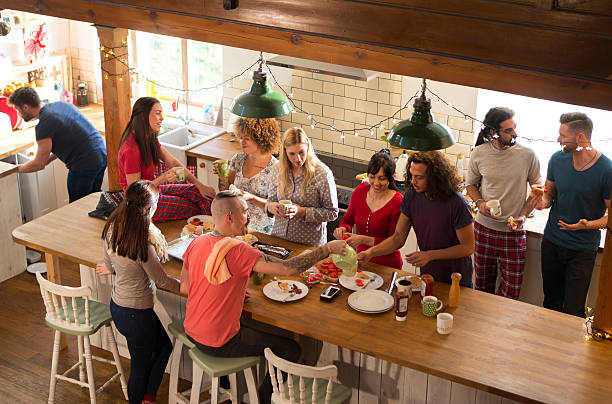 Weekend Away with Friends A group of friends are preparing breakfast in the kitchen, they are eating bacon sandwiches and chatting happily amongst themselves. It looks like they are on a weekend away vacation. roommate stock pictures, royalty-free photos & images