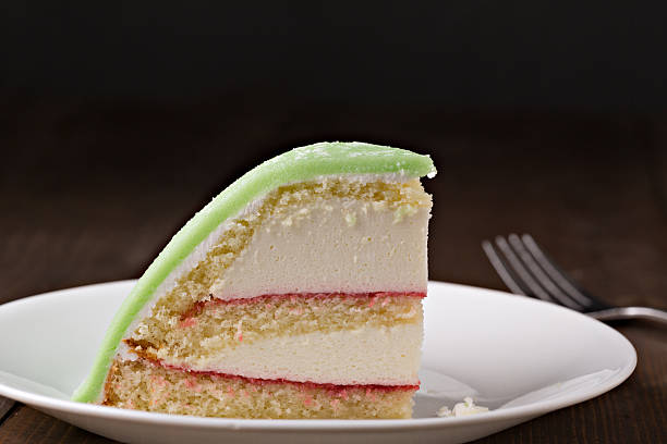 Slice Of Swedish Princess Cake An extreme close up horizontal photograph of a slice of traditional Swedish Princess Cake. It consists of alternating layers of white cake, and pastry cream separated by thin layers of jam then it is topped with a green layer of green marzipan. The cake is isolated on black providing plenty of room for copy space. marzipan stock pictures, royalty-free photos & images