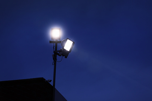 Floodlights and a CCTV camera provide security at a factory. Ample copy space on the dark blue nighttime sky.