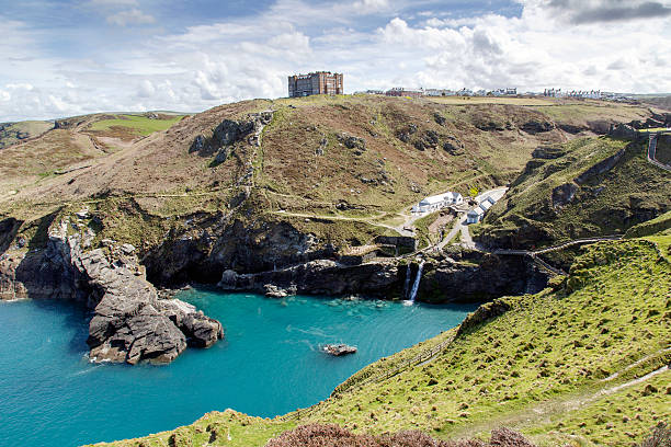 Tintagel Castle - Entrance Tintagel, Cornwall, UK: April 14, 2016: A view of the main entrance to Tintagel Castle in the valley and Hotel Camelot on the cliff. There is a  beach cafe, visitors centre, public facilities and the booking desk and the entrance. The castle is maintained by English Heritage who are also responsible for Stonehenge and many other ancient sites across England. box office photos stock pictures, royalty-free photos & images