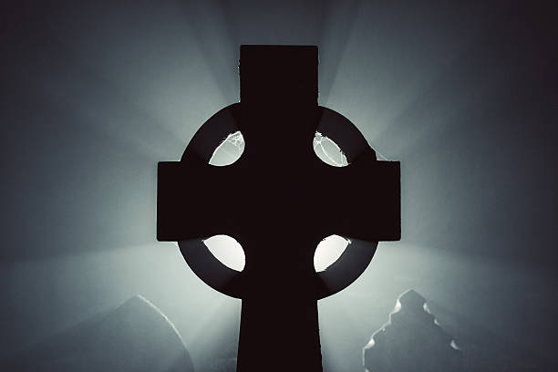 A 19th century celtic cross tombstone is backlit in heavy fog.  Long exposure.