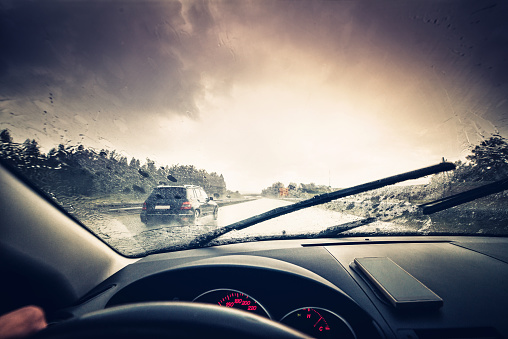 A car driving through a rainy highway with the windshield wipers in motion.