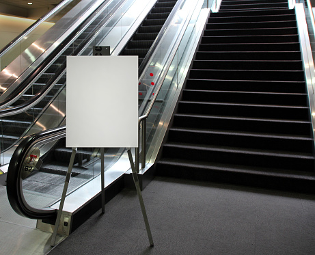 Blank poster on an easel at the base of an escalator and stairs