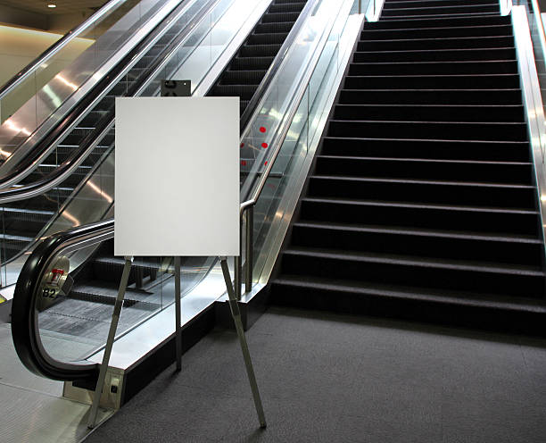 Blank easel sign at the base of an escalator Blank poster on an easel at the base of an escalator and stairs meeting sign stock pictures, royalty-free photos & images