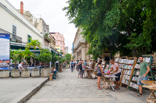 Havana, Cuba - December 10, 2015:  Tourists buying painting and books at stands on the Plaza de Armas in Havana. Stands with books and pictures are a tourist attraction.