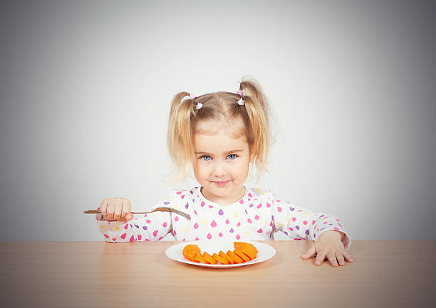 小さな女の子 食べる ニンジンと分岐点があります。 - cute disgust carrot caucasian ストックフォトと画像